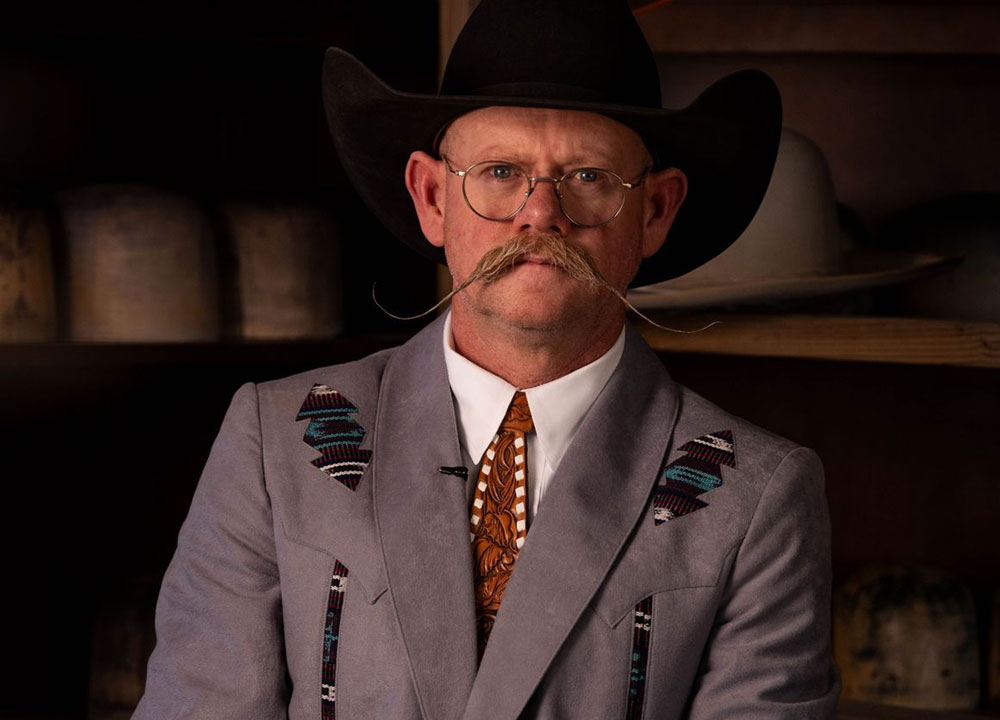 A man, Chaz Mitchell, standing in front of his hat bar and his hat tools.